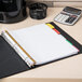 A binder with Avery Big Tab multi-color dividers on a desk with papers and a calculator.
