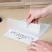 A hand opening a Universal clear laminating pouch to reveal a piece of paper with the word "lunch"