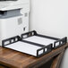 A black Universal side load desk tray holding white paper on a wood desk with a printer.