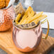 A close up of an American Metalcraft copper Moscow Mule mug filled with french fries and chicken.