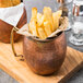 An American Metalcraft hammered antique copper Moscow Mule mug filled with french fries on a table.