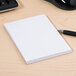 A white Universal unruled scratch pad with white paper on a wood surface with a pen.