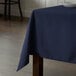 A wooden square table with a navy blue Intedge cloth table cover on it.