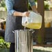 A woman pouring Admiration Canola Frying Oil into a metal pot.