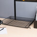 A black Universal mesh tray on a table with a notebook and pen.
