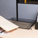 A black Universal stackable mesh tray on a desk with a computer and a folder.