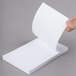 A hand holding a Universal white scratch pad sheet.