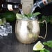 A person pouring a drink from a bottle into an American Metalcraft Mirrored Gold Moscow Mule Mug.