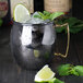 An American Metalcraft mirrored black Moscow mule mug filled with ice and lime slices on a wooden surface.