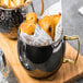 An American Metalcraft mirrored black Moscow Mule mug filled with fried food on a table.