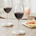 Two Acopa Select Blanc wine glasses filled with red wine on a table with food.
