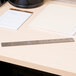 A Universal stainless steel ruler with cork back and black numbers sitting on a desk next to a notebook.