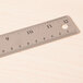 A Universal stainless steel ruler with cork back on a wood surface with 1/16" scale markings.