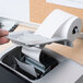 A hand inserting a roll of Universal Office white 1-ply paper into a printer.
