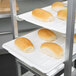 A Winholt stainless steel platter cart holding trays of bread on a shelf.