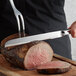 A Vollrath stainless steel knife slicing a piece of meat.