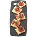 A rectangular black Cal-Mil flat bread serving board with cheese and tomatoes on it.