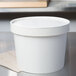 A white Huhtamaki paper food container with a lid on a counter.