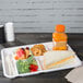 A white Huhtamaki Chinet cafeteria tray with food including a sandwich, fruit, and a bottle of juice.