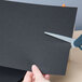 A person using scissors to cut a piece of Astrobrights Eclipse Black cardstock.