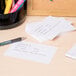 A group of white Universal ruled index cards on a desk with pens and highlighters.