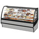 A True refrigerated bakery display case with different cakes and pastries behind curved glass.