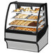 A True curved glass stainless steel dry bakery display case on a counter with various pastries.