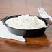 A black Dart foam casserole dish filled with mashed potatoes and a fork on a white background.