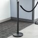 A Lancaster Table & Seating black metal crown top crowd control stanchion with a rope around the pole.
