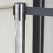 A Lancaster Table & Seating stainless steel crowd control stanchion with a black retractable belt.
