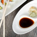 A white porcelain divided dish with sushi and soy sauce on one side and chopsticks on the other.