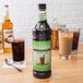 A bottle of Monin Unsweetened Cold Brew Coffee Concentrate on a table with a glass of the liquid.