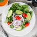 A white wide rim porcelain plate with a salad of cucumbers, tomatoes, and onions.