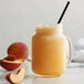 A glass jar with a straw filled with peach smoothie and peach slices.