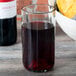 A clear Arcoroc wine tumbler filled with red liquid on a table next to a bowl of cheese.