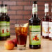 A bottle of Monin Peach Tea 7:1 Concentrate on a table with a glass of iced tea and ice cubes.