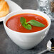 A bowl of tomato soup with basil leaves in a Reserve by Libbey white porcelain bouillon bowl.
