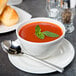 A Reserve by Libbey white porcelain bouillon bowl filled with tomato soup with a spoon and bread.