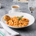 A Reserve by Libbey Royal Rideau white porcelain bowl filled with pasta on a table with a cup of coffee.