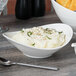 A white porcelain bowl filled with mashed potatoes and spices with a spoon.