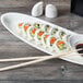 A plate of sushi on a white Libbey porcelain tray with chopsticks and soy sauce.