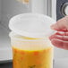 A hand holding a ChoiceHD translucent plastic deli container with soup in front of a microwave.
