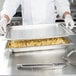 A chef in a white coat using a Vollrath stainless steel food transport cover on a large rectangular tray of french fries.