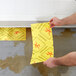 A person using a Spilfyter yellow absorbent pad to clean up a spill.