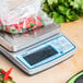 An Edlund BRAVO! digital portion scale on a table with a bag of red peppers and other vegetables.