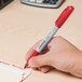 A hand using a Universal red bullet tip permanent marker to write on a piece of paper.