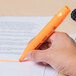 A hand using a Universal fluorescent orange highlighter to mark a piece of paper.