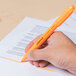 A hand holding a Universal Fluorescent Orange Chisel Tip Highlighter pen over a paper.