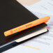 A Universal fluorescent orange highlighter pen on a black notebook.