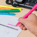A hand holding a Universal pink chisel tip highlighter over a paper with colorful pens.